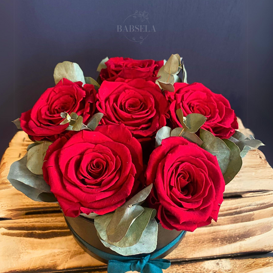 Close-up of a bouquet of vibrant red preserved roses arranged with eucalyptus leaves in a round box, designed by Babsela