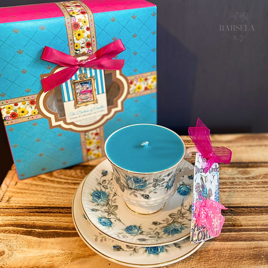 1970s Royal Turquoise Rose Tea Candle in a floral teacup with matching saucer, placed on wood, with a blue gift box and pink ribbon