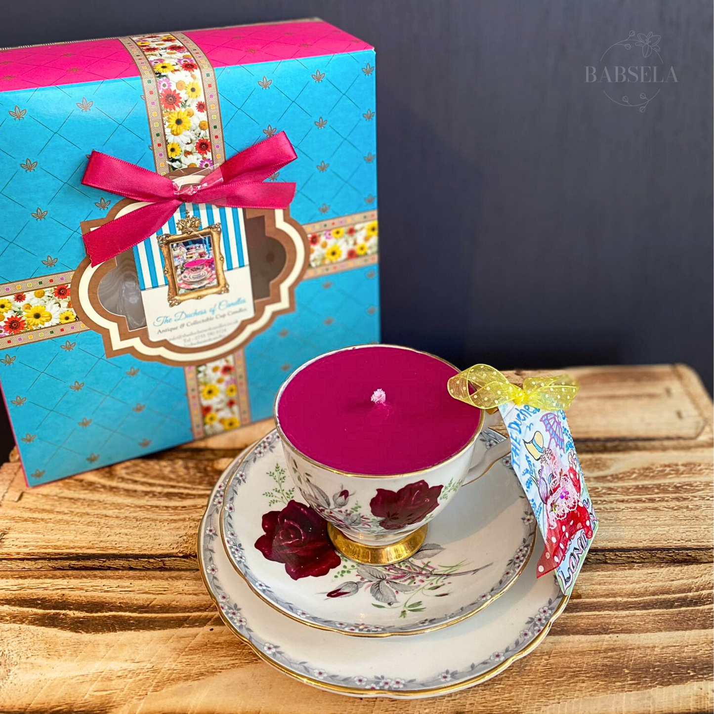 1960s Royal Stafford Candle in a floral teacup with matching saucer, placed on wood, with a blue gift box tied with a pink ribbon