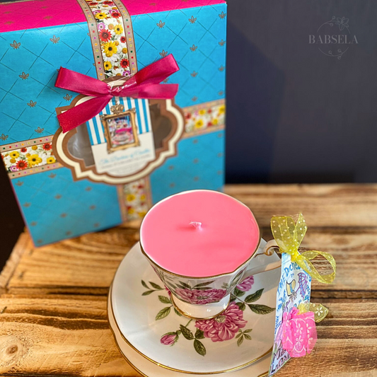 1960s Roslyn Rosa Fruity Tea Candle in a floral teacup with matching saucer, placed on wood, with a blue gift box and pink ribbon behind